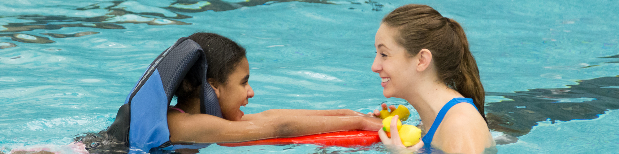Student plays with young child in the pool.